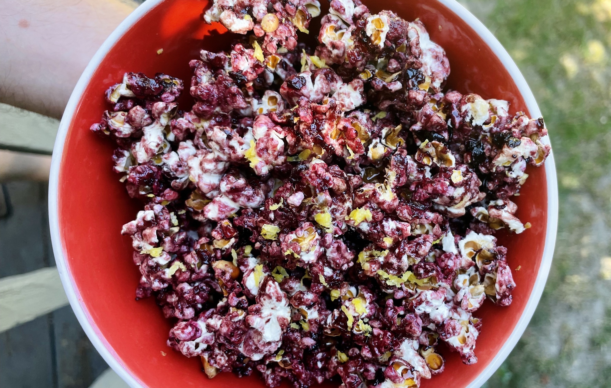 Photograph of a red bowl of Blueberry Pancake Craft Popcorn taken outdoors from directly above