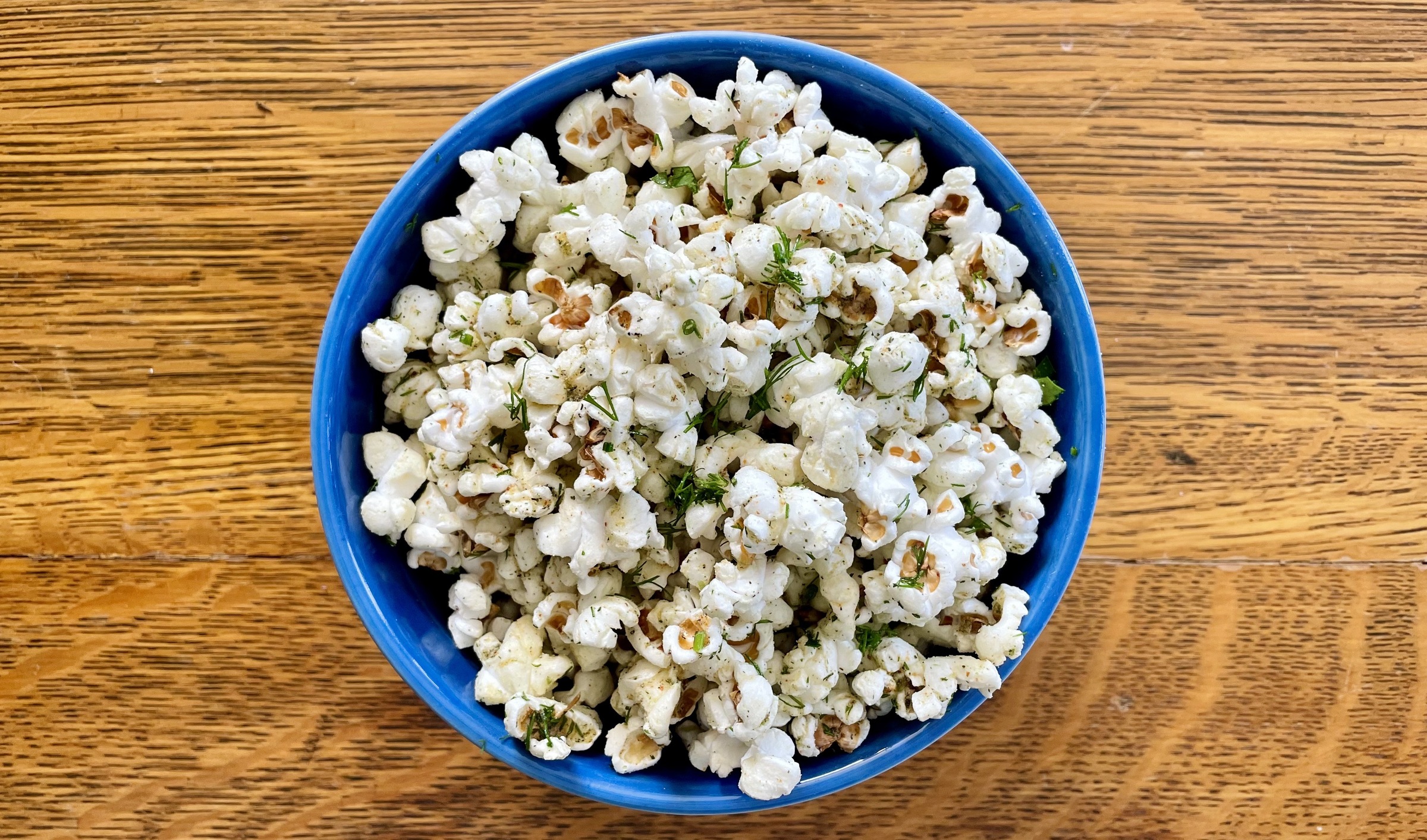 Photograph of a blue bowl of Habanero Ranch Craft Popcorn on a wooden surface taken from directly above